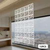 A white decorative screen made of interlocking square panels with circular cutouts, positioned in front of a window overlooking a cityscape. Náhled obrázku produktu
