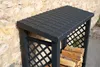 A dark gray plastic log store with a tiled roof, positioned against a stone wall. Some firewood is visible inside. Produktbild-Vorschau