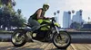 A person wearing a helmet and riding a motorcycle on a wooden pier with buildings and palm trees in the background. Produktbild-Vorschau