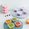 A collection of small, square food storage containers filled with colorful purees and fruits, arranged on a light blue surface. Produktbild-Vorschau