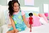 A young girl sitting on a bed, holding a Barbie doll. Podgląd zdjęcia produktu