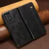 A close-up shot of a black leather flip wallet phone case for a Samsung Galaxy A52S 5G, resting on a brown leather surface with tan leather rolls in the background. Produktbild-Vorschau