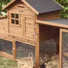 A wooden chicken coop with an attached run, set in a grassy outdoor environment with some foliage in the background. A wicker basket with eggs is in the foreground. Produktbild-Vorschau