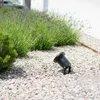 A black LED garden spotlight is placed on a bed of light-colored gravel next to a lavender bush. Produktbild-Vorschau
