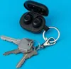A pair of black wireless earbuds in their charging case, attached to a keychain with three silver keys, on a blue background. Anteprima dell’immagine prodotto