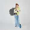 A young girl stands with a backpack on her shoulders, holding a water bottle. Produktbild-Vorschau
