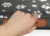 A hand is holding a brown tag on a gray dog bed with paw prints. Produktbild-Vorschau