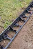 A black plastic garden edging is installed along a garden bed, separating the soil from the grass. Produktbild-Vorschau