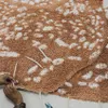 A close-up view of a person's hands working on a brown rug with white spots, possibly a deer pattern. Voir les images du produit