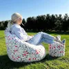 A woman relaxing on a floral bean bag chair with a matching ottoman in a grassy outdoor setting. Náhľad obrázku produktu