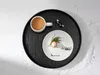 A festive winter scene with a mug of coffee and a dessert plate on a black tray, surrounded by artificial snow. Produktbild-Vorschau