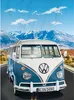 A vintage blue and white Volkswagen bus driving on a road with mountains in the background. Produktbild-Vorschau