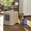A cat stands next to a litter box and a blue accessory on a wooden floor, with outdoor furniture and plants in the background. Produktbild-Vorschau