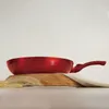 A red frying pan is placed on a wooden board with some wheat stalks and a cloth. Náhled obrázku produktu