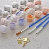 A paint-by-numbers kit with numbered paint pots, brushes, and hanging hardware laid out on a canvas with printed numbers. Produktbild-Vorschau