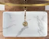A top-down view of a rectangular white sink with marble-like gray veining, featuring a gold faucet. The sink is placed on a wooden surface, with a golden rim visible above. Anteprima dell’immagine prodotto