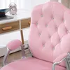 A close-up of a pink velvet office chair with silver accents, placed next to a white desk with a laptop and a pink alarm clock. Produktbild-Vorschau