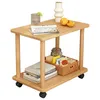 A wooden side table with two shelves and wheels, decorated with a glass of water, fruit, books, and a basket of items. Produktbild-Vorschau
