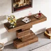 A wooden console table with a unique stacked design, placed against a white wall with a painting above it. A bouquet of flowers and a magazine are on top of the table, along with a glass and a bottle of liquor on a tray. Two vintage suitcases are stacked o Anteprima dell’immagine prodotto