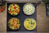 A top-down view of a stovetop with four dishes of food. Produktbild-Vorschau