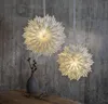 Two paper star lanterns hang against a textured concrete wall, with a vase and dried branches on a wooden surface below. Podgląd zdjęcia produktu