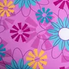 A close-up, flat lay view of a pink fabric with a repeating pattern of stylized flowers in yellow, teal, and magenta. Produktbild-Vorschau