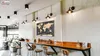 A modern cafe interior with a long wooden counter, stools, and wall decor. Náhľad obrázku produktu
