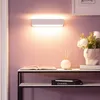 A white LED wall light is mounted on a purple wall above a shelf with decorative items. Produktbild-Vorschau