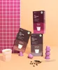 Three boxes of coffee capsules are stacked, with some loose capsules and coffee beans scattered around. A cup of coffee is also present. Anteprima dell’immagine prodotto