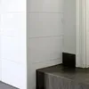 A corner view of a modern interior, showing white paneling and a dark wood bench. Anteprima dell’immagine prodotto