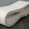A white, curved scratching board for cats, placed on a dark wooden floor with a gray textured wall in the background. Produktbild-Vorschau