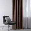 A dark brown curtain hangs next to a sheer white curtain, with a gray armchair and pillow in the foreground. Podgląd zdjęcia produktu