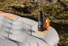 A black Flextail Zero Pump mini air pump with an orange attachment is placed on a gray inflatable sleeping pad outdoors. Podgląd zdjęcia produktu