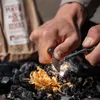 A person is using a fire starter to ignite tinder over charcoal. Produktbild-Vorschau
