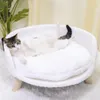 A cat is lying on a white, fluffy pet bed with wooden legs. Náhled obrázku produktu