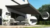 A dark gray retractable awning is extended over a patio with outdoor furniture. Several circular insets highlight details of the awning, including its remote control, LED lighting, and scalloped edge. Produktbild-Vorschau