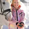 A woman in a pink puffer jacket is holding a handful of horse feed next to a white horse. Podgląd zdjęcia produktu