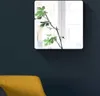 A framed mirror with a plant branch in front of it, hanging on a dark blue wall above a yellow chair. Anteprima dell’immagine prodotto