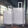 Two suitcases covered in clear protective covers are standing in an airport or modern building hallway. Anteprima dell’immagine prodotto