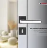 A close-up of a black and white door handle set on a door, with a blurred interior scene in the background. Produktbild-Vorschau