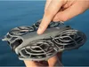 A hand is pressing a button on a gray drone, which is held over a blue body of water. Produktbild-Vorschau