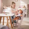 A young girl is playing with a doll in a high chair, brushing its hair, in a bedroom setting. Náhľad obrázku produktu