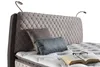 A close-up view of a bed with a tufted headboard and pillows. Produktbild-Vorschau
