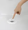 A hand is pressing down on a white bathtub drain stopper and hair catcher. Voir les images du produit