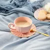 A pink teacup and saucer with a golden spoon and macarons on a blue blanket. Produktbild-Vorschau