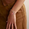 A close-up shot of a person's arm wearing a silver charm bracelet with a pink gummy bear charm and a circular silver charm. Anteprima dell’immagine prodotto