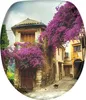 A charming, narrow cobblestone street in a European village, adorned with vibrant purple bougainvillea cascading over old stone buildings. A black cat walks along the street. Anteprima dell’immagine prodotto