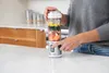 A person is using a portable blender filled with fruits and vegetables in a kitchen. Podgląd zdjęcia produktu