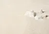 Several small white rocks are scattered on a light beige, textured surface. Produktbild-Vorschau
