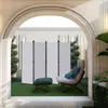 A white folding screen divider is set up on a green lawn in an outdoor patio area, with a chair and ottoman nearby. Produktbild-Vorschau